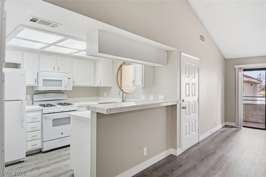 830 N Sloan Lane, #202, Las Vegas, NV 89110 An open kitchen with white cabinetry and a tiled breakfast bar connects to the living area.
