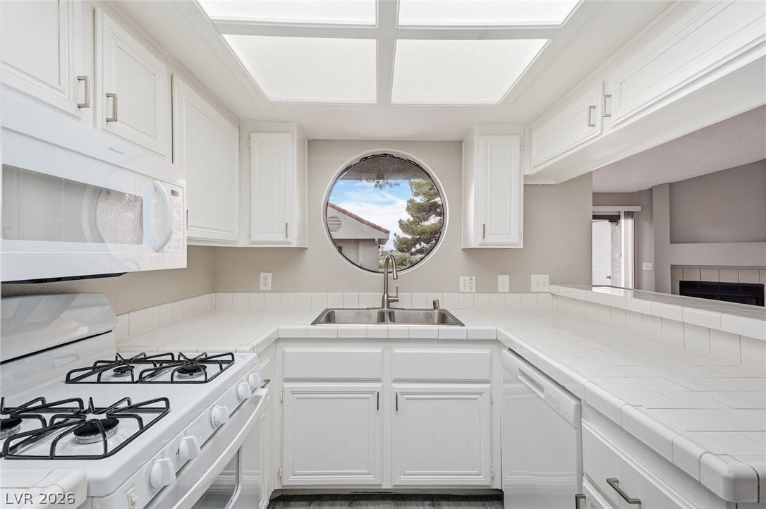 830 N Sloan Lane, #202, Las Vegas, NV 89110 An architectural round window centers this kitchen featuring classic tiled countertops and white cabinetry.