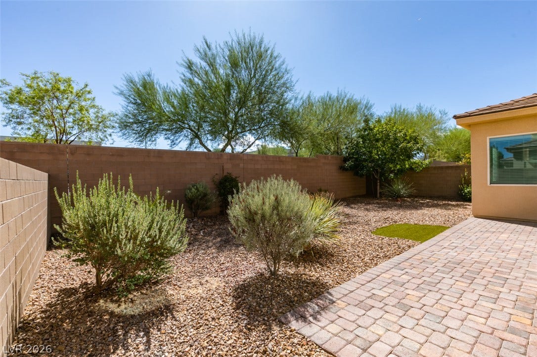 Low-maintenance desert landscaping borders a spacious brick paver patio under open blue skies.