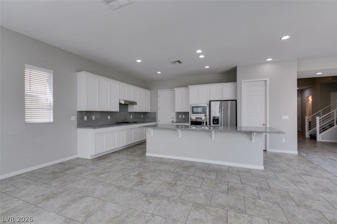 An open kitchen area features sleek tile flooring, stone countertops, and extensive cabinetry.