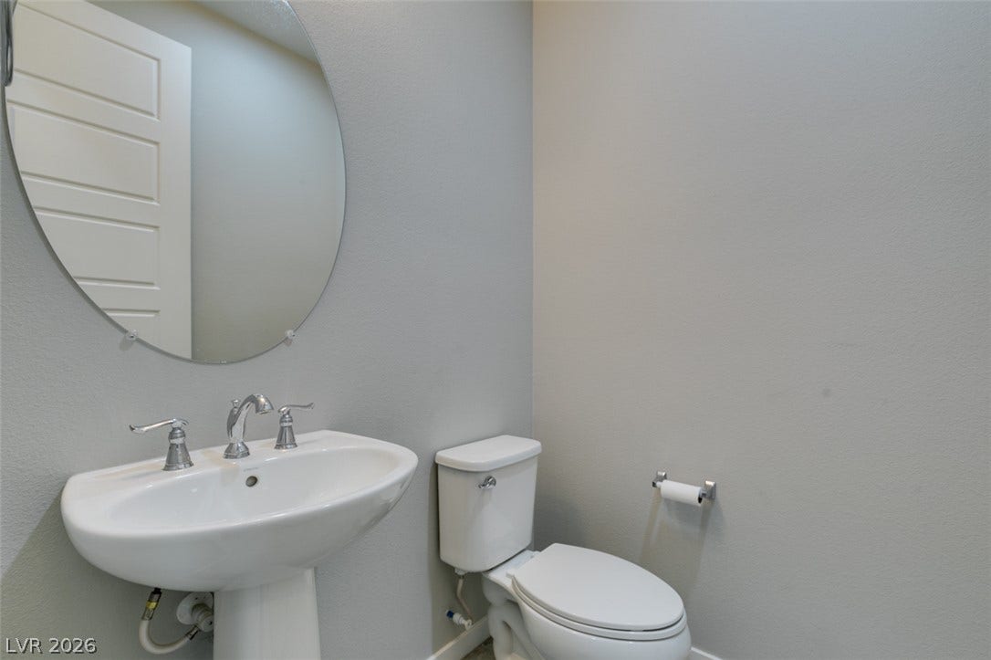 A clean half-bath features a classic pedestal sink under a round mirror.