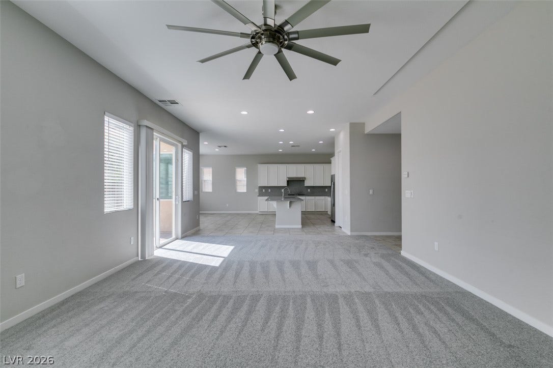An open floorplan connects the carpeted living area to the distant tile-floored kitchen.
