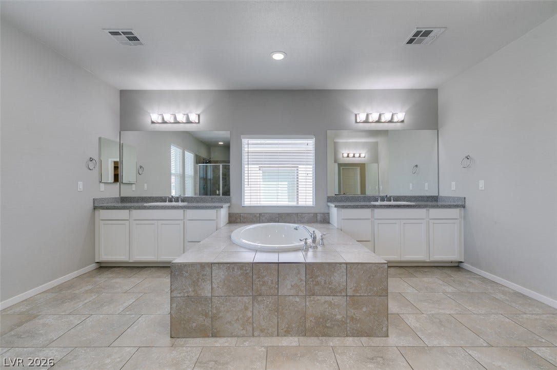 Dual vanities flank a central tile-surrounded soaking tub on tile floors.