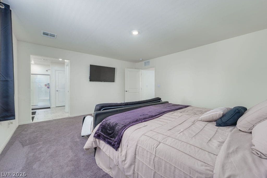 6135 Larimar Gold Street, North Las Vegas, NV 89115 A spacious bedroom features plush carpeting and an adjacent en suite bathroom.