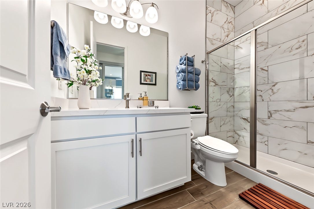 A glass-enclosed shower featuring marble-look tile highlights this modern bathroom.