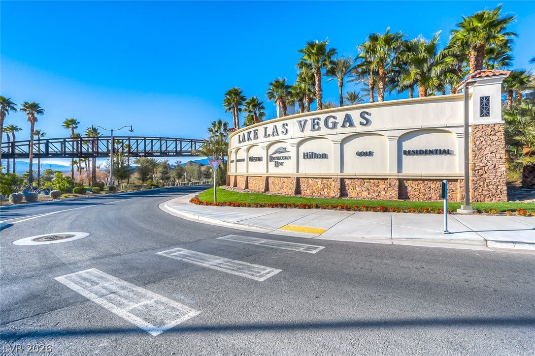 A grand community entrance monument stands framed by towering palm trees under clear blue skies.