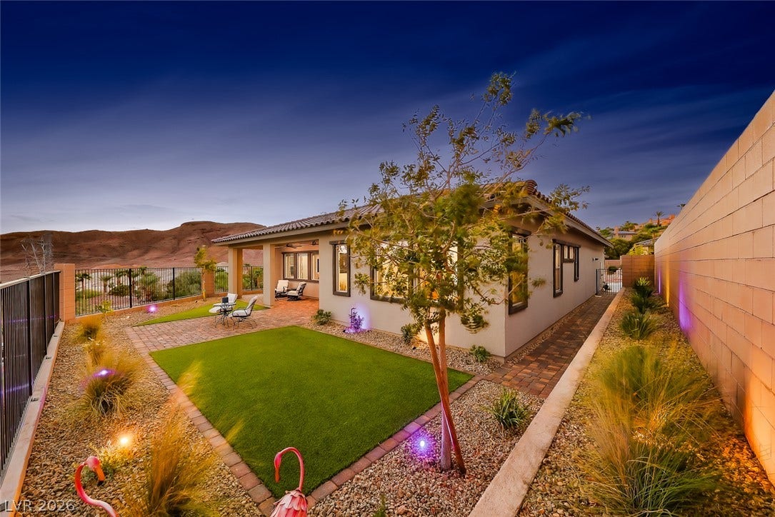 Desert mountains rise behind this beautifully landscaped backyard featuring a manicured lawn and covered patio.