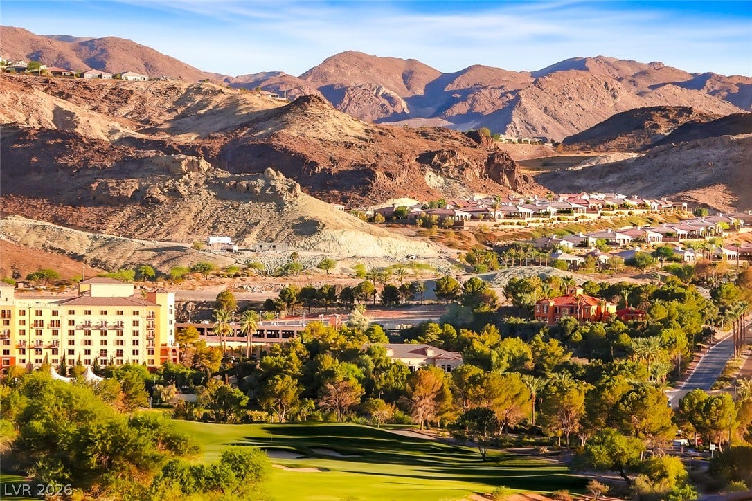 Dramatic mountain ranges frame a verdant golf course community under a bright blue sky.