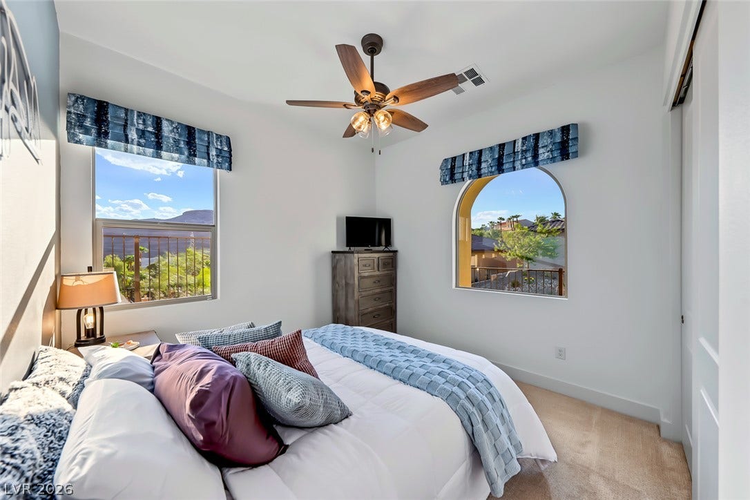 Natural light pours through dual windows in this carpeted bedroom featuring distant hillside views.