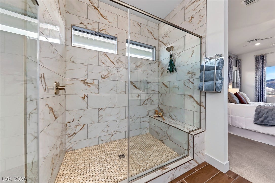 A glass-enclosed walk-in shower showcases elegant marble-patterned tile and a built-in bench.