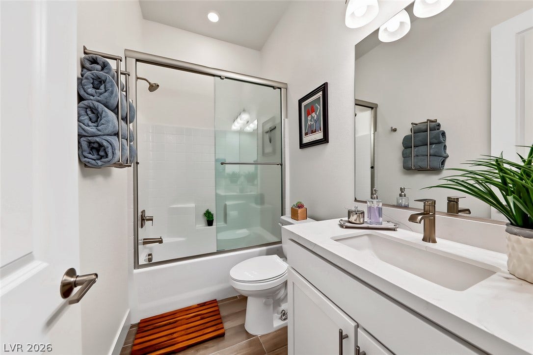 A glass-enclosed shower and tub combination stands opposite a sleek single-sink vanity with stone counters.