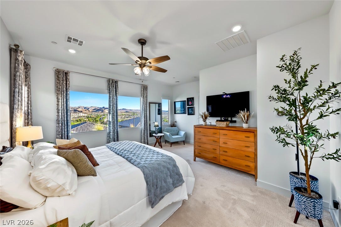 Large windows frame picturesque desert and mountain views in this carpeted bedroom.