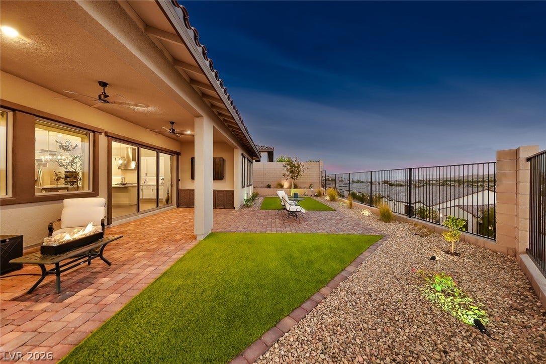 An expansive paved patio overlooks a beautifully landscaped yard beneath a desert twilight sky.