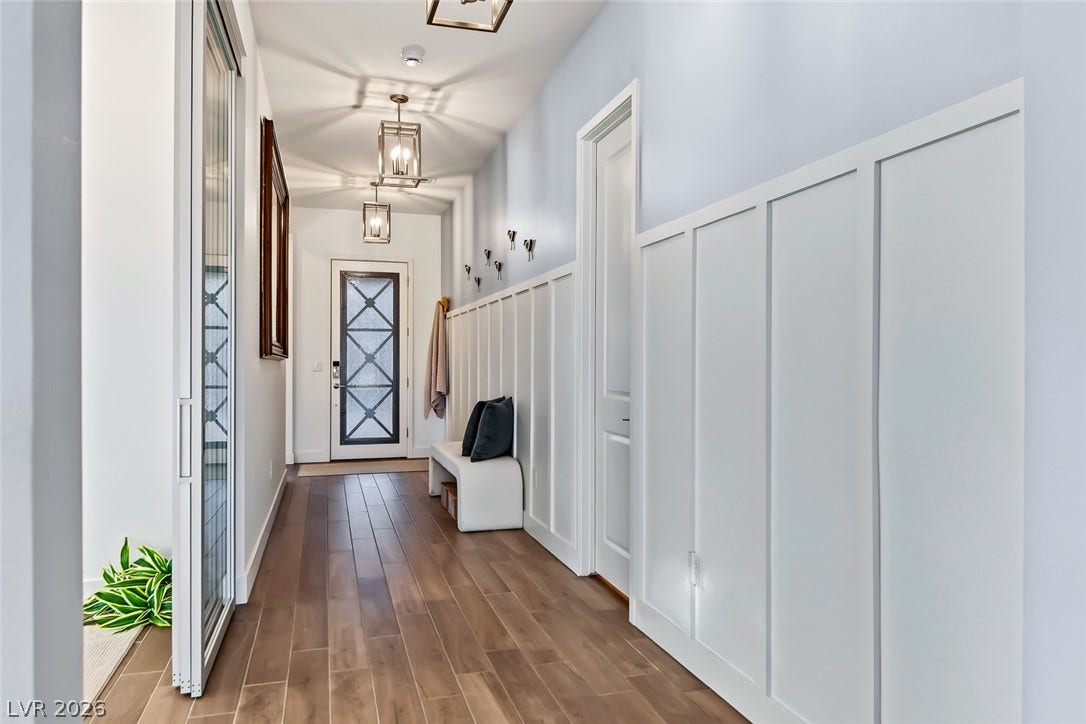 Rich wood-look flooring guides visitors through a bright hallway featuring classic board and batten wainscoting.