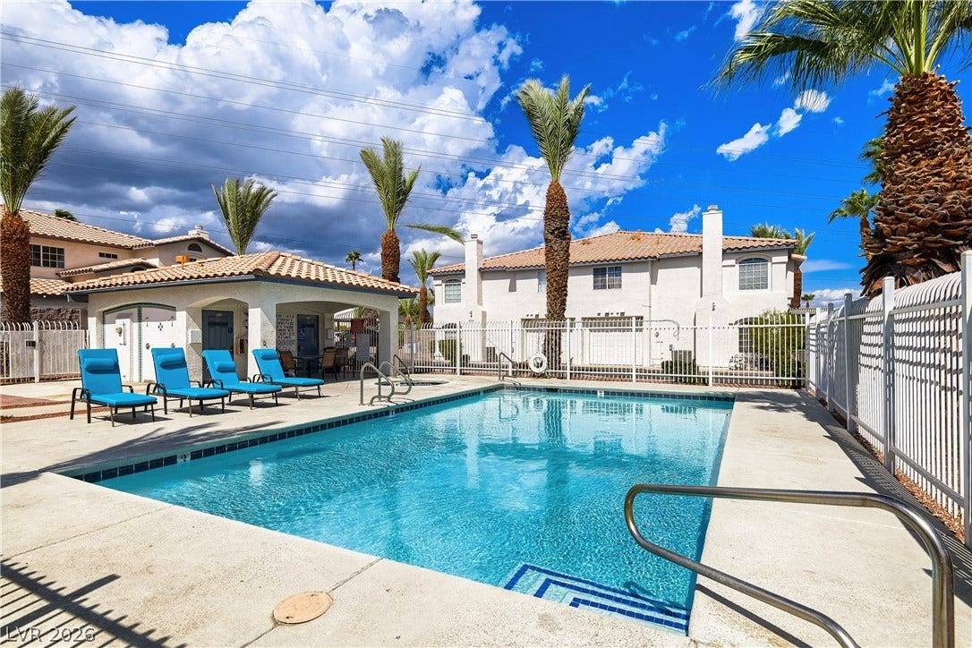 An inviting swimming pool is bordered by concrete decking and tall palm trees.