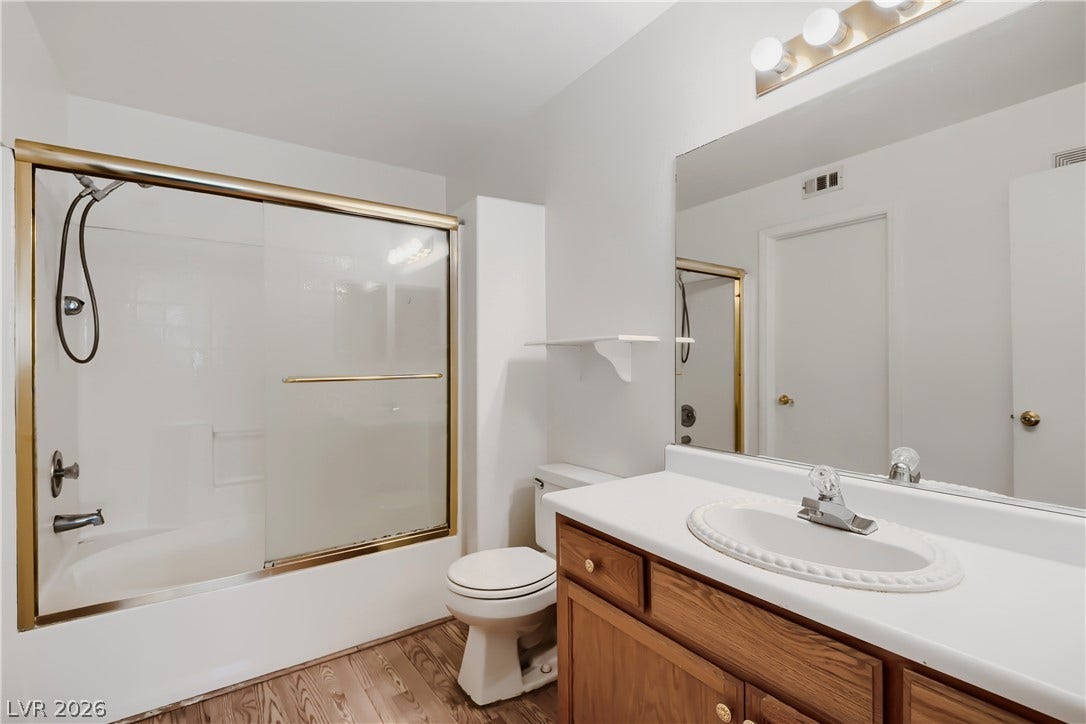 Warm wood flooring pairs beautifully with classic cabinetry in this tidy full bathroom.