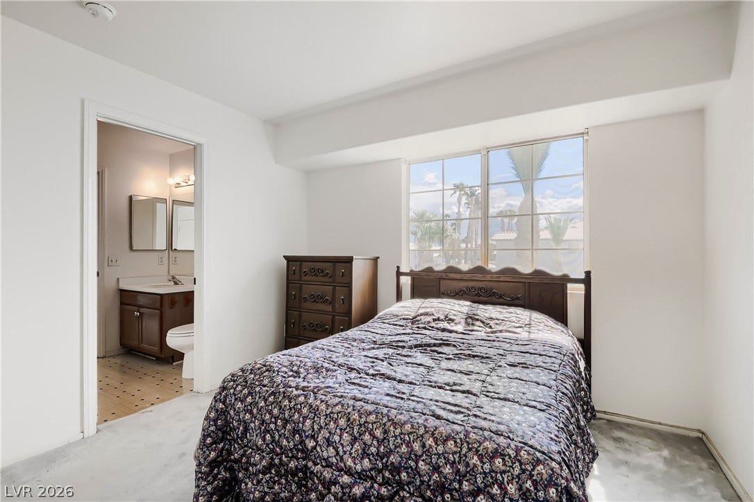 An ensuite bathroom accesses this bedroom featuring a large window framing palm tree views.