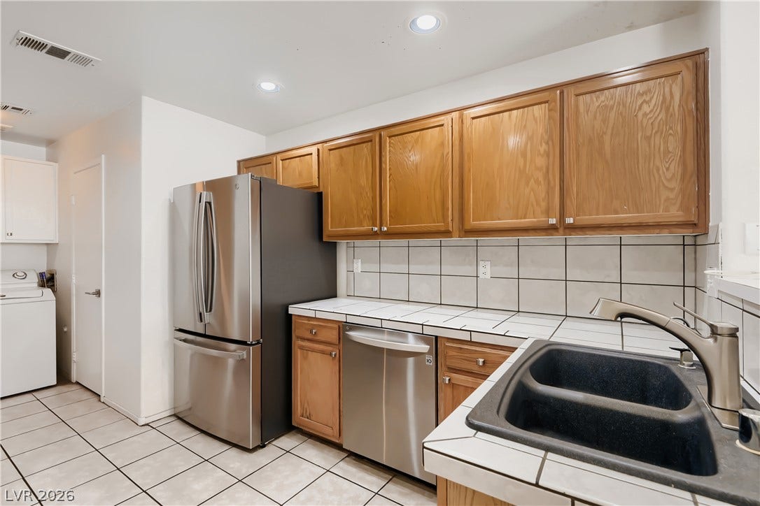 Functional workspace features classic tile countertops, natural wood cabinetry, and modern stainless appliances.