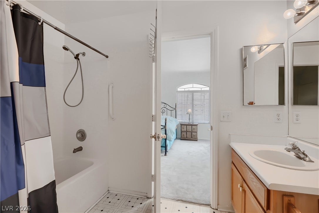An open doorway links the bathroom to an adjacent carpeted bedroom featuring arched window details.
