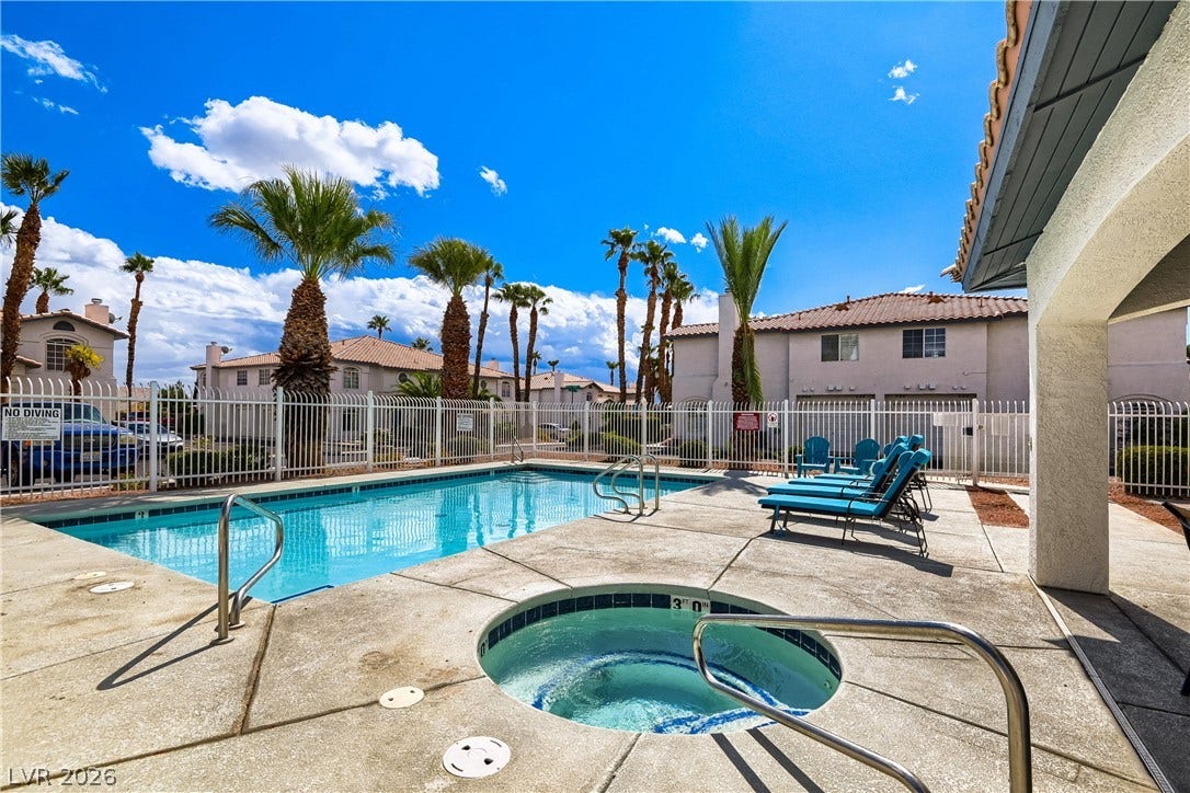 A sparkling swimming pool and adjacent spa sit surrounded by a concrete patio and fencing.