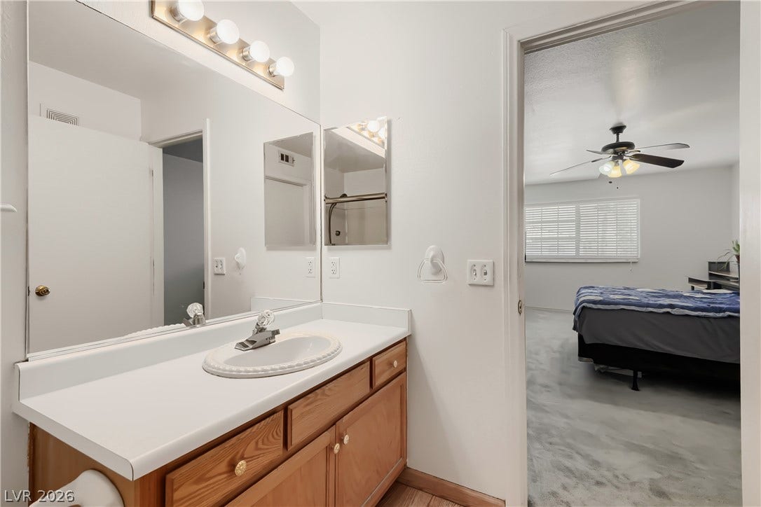 An open doorway links the wood vanity bathroom directly to an adjacent carpeted bedroom.