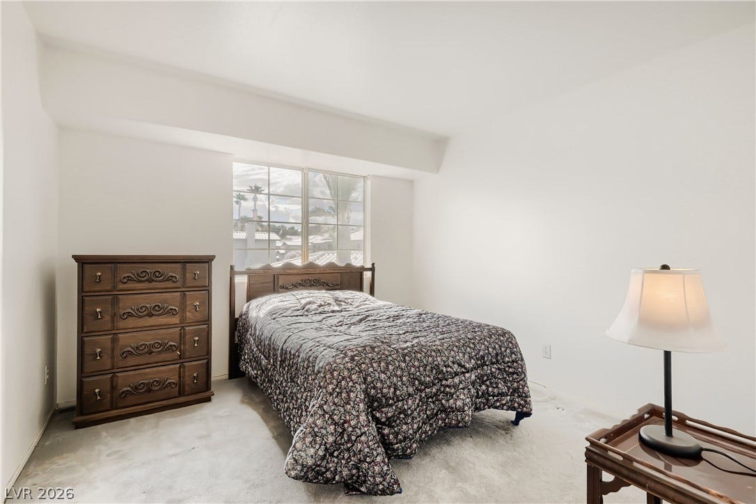A multi-pane window frames neighborhood views, illuminating the carpeted bedroom.