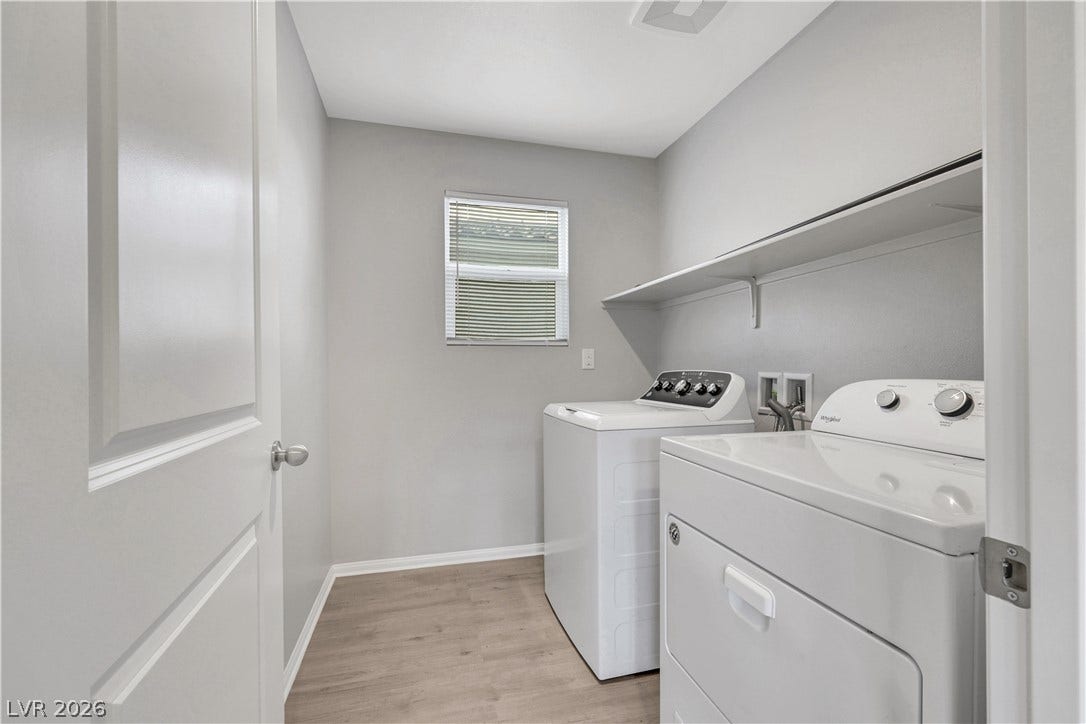 Functional laundry room features overhead open shelving and durable wood-look flooring.
