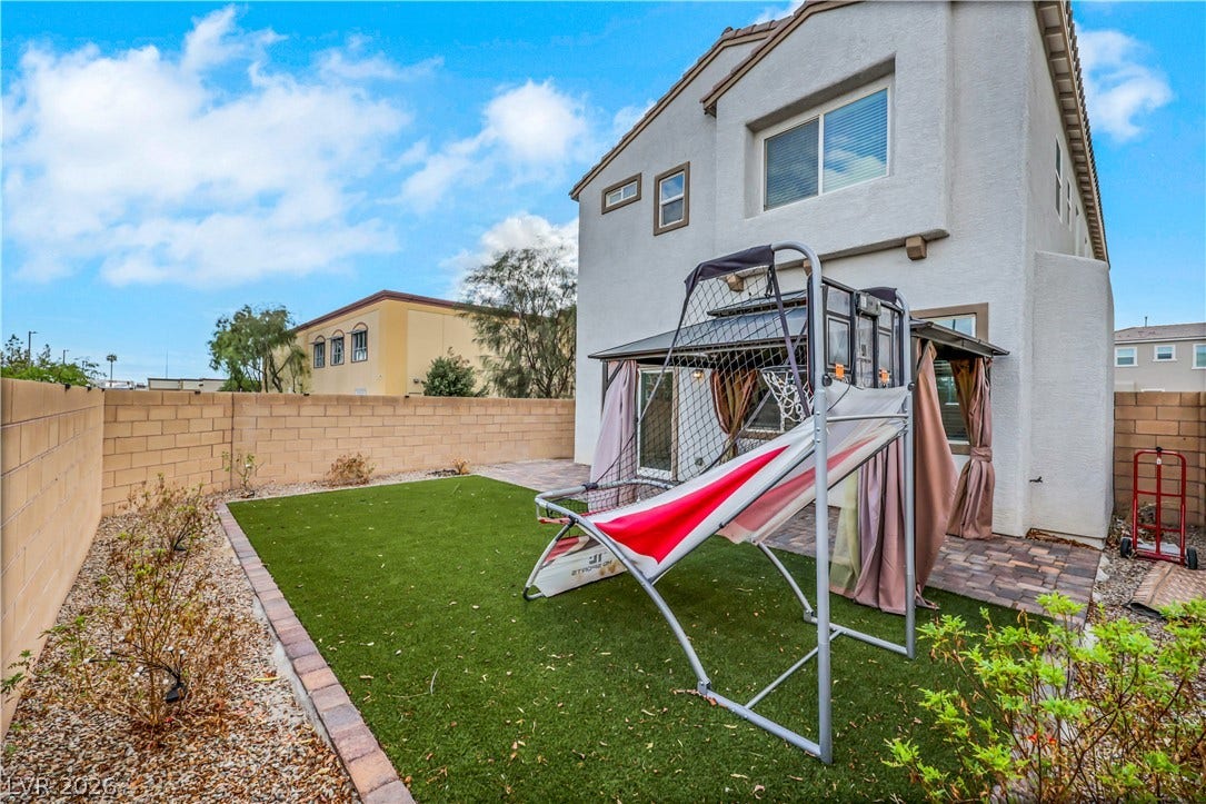 An inviting backyard features a paved patio area bordered by synthetic green grass.
