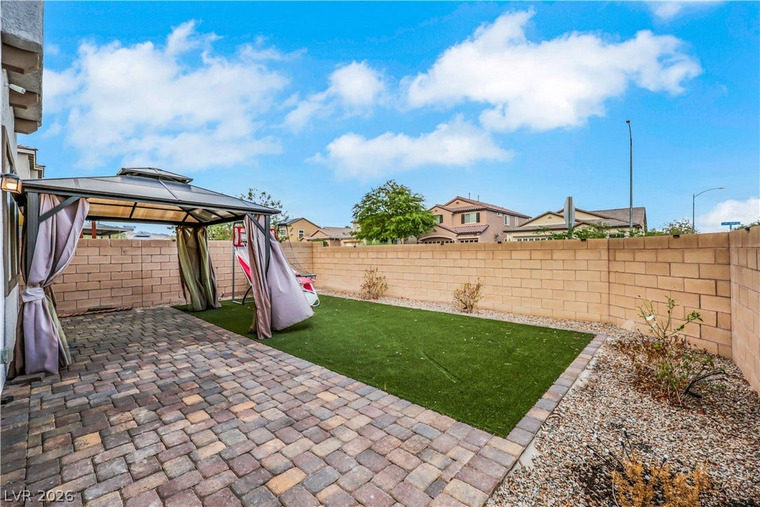 An inviting backyard features a paved patio area bordered by synthetic green grass.