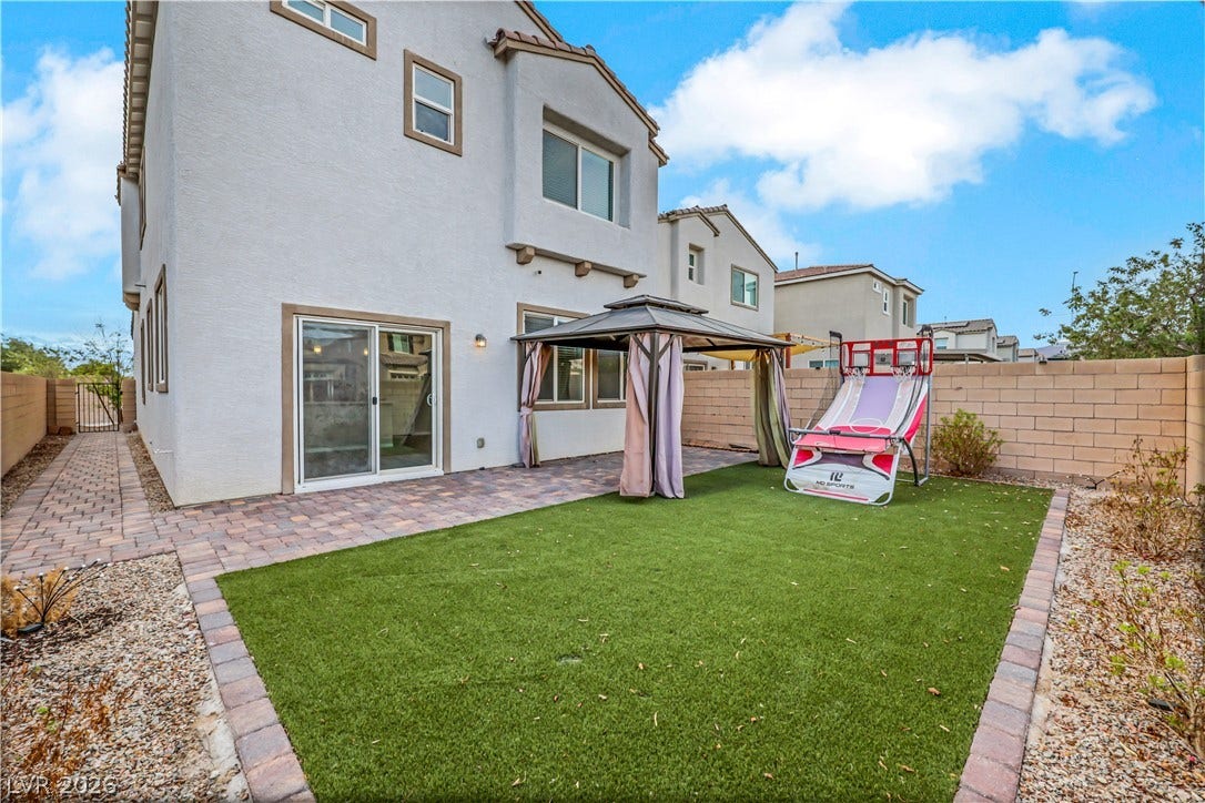 An inviting backyard features a paved patio area bordered by synthetic green grass.