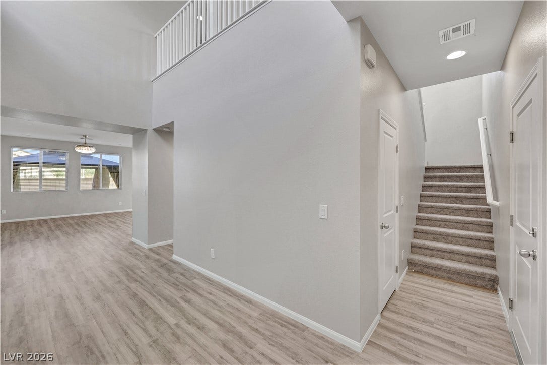 An inviting entrance foyer showcases double-height ceilings, durable vinyl plank flooring, and a carpeted staircase.