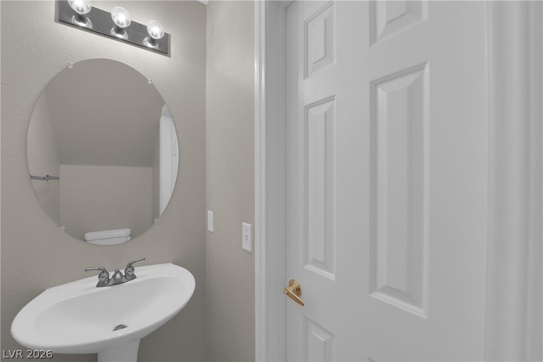 1158 Ekalaka Road, Henderson, NV 89052 A classic pedestal sink sits beneath a round mirror in this compact powder room.
