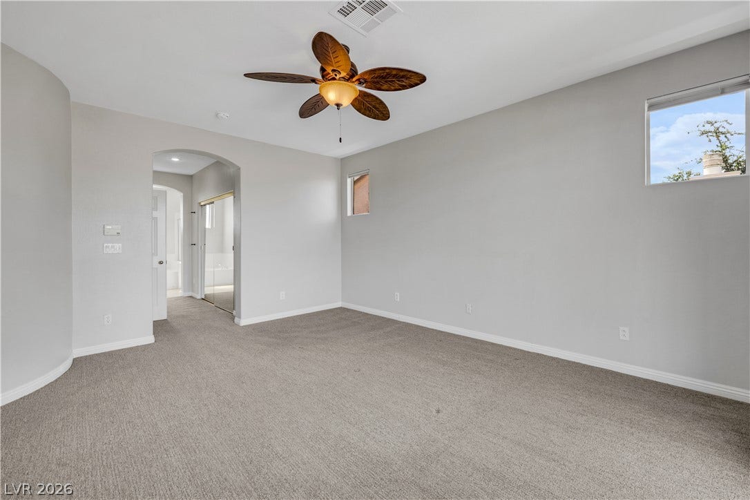 An arched doorway leads into this spacious bedroom featuring plush carpeting and neutral walls.