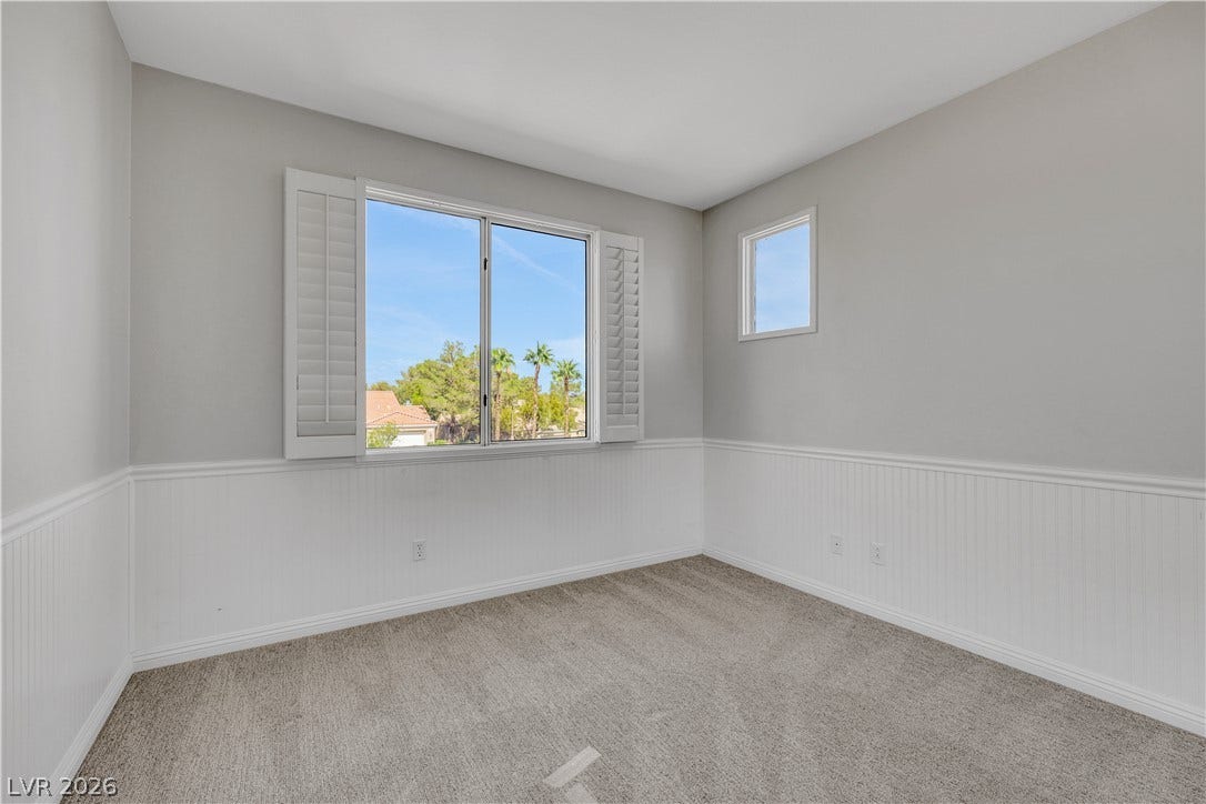 Plentiful natural light fills a versatile bedroom featuring classic beadboard wainscoting and cozy carpeting.