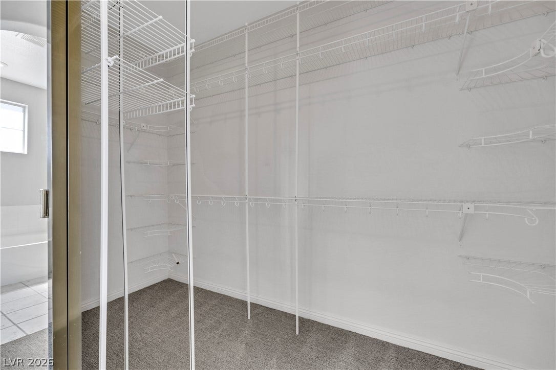 Ample wire shelving lines this functional walk-in closet featuring carpeted flooring.