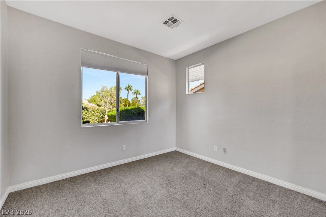 Sunlight streams through a large window overlooking the neighborhood in this cozy carpeted bedroom.