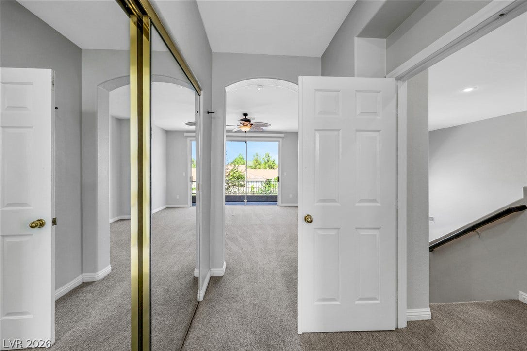 An arched doorway leads into a light-filled bedroom featuring soft carpeting and a private balcony.