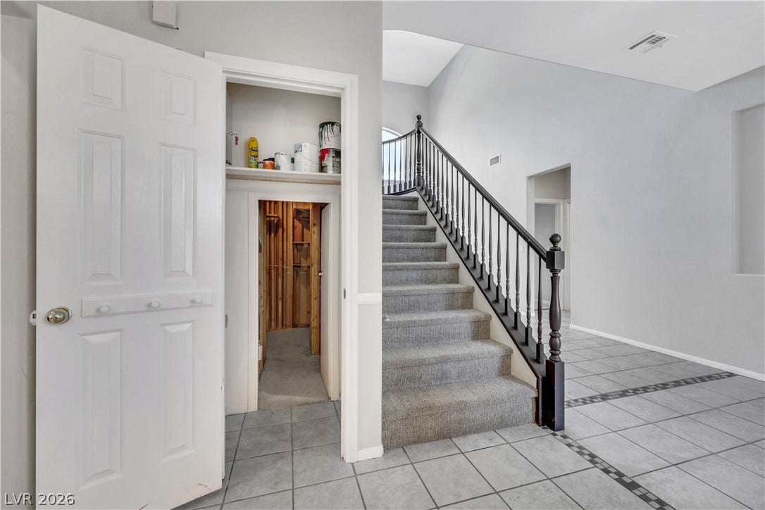 Tiled flooring and a carpeted staircase with a dark wooden handrail define this entryway.