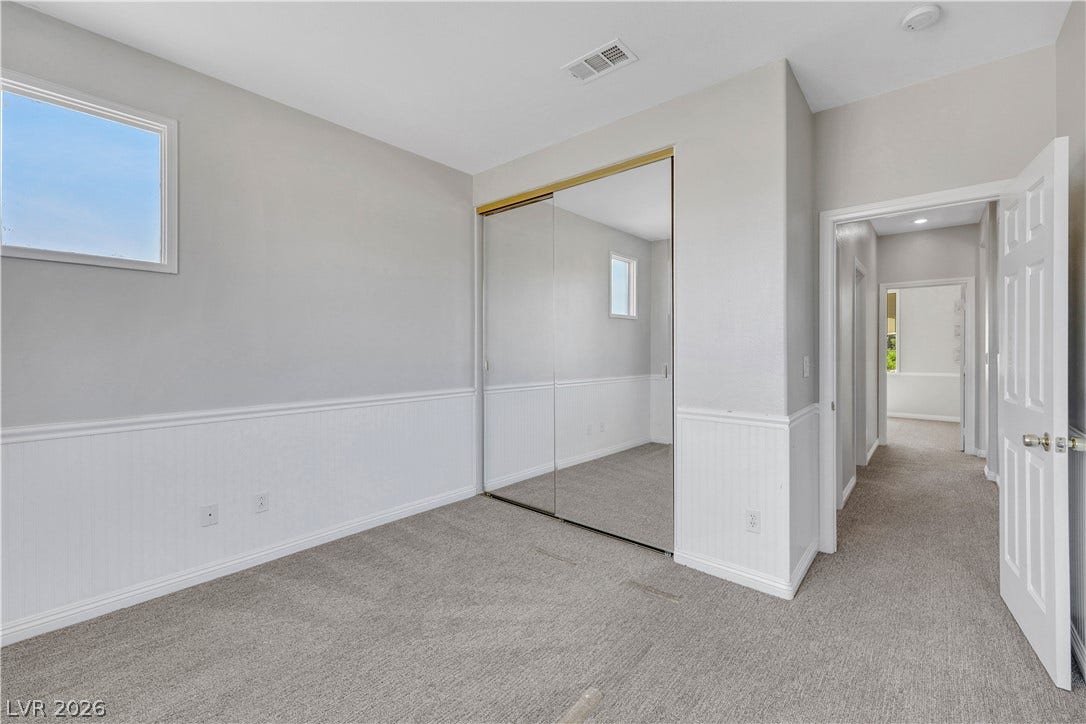 Classic wainscoting trims this bedroom featuring plush carpeting and sliding mirrored closet doors.