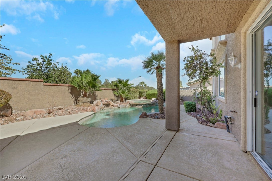 A shaded patio looks out over a private backyard pool surrounded by desert plantings.