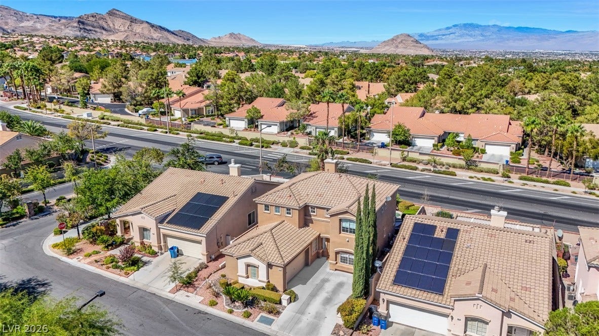 Elevated view reveals tile roofs, paved driveways, and solar panels against a mountain backdrop.