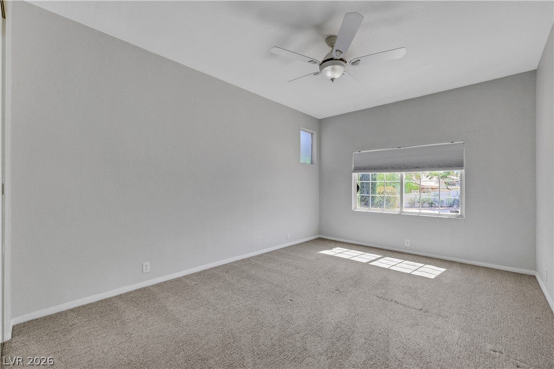 Natural light streams across the carpeted floor of this spacious bedroom.