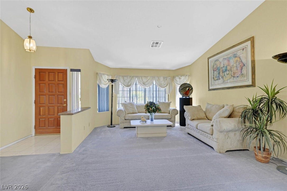 805 Stillwater Lane, Henderson, NV 89014 Vaulted ceilings and broad windows frame this carpeted living room adjacent to the entryway.