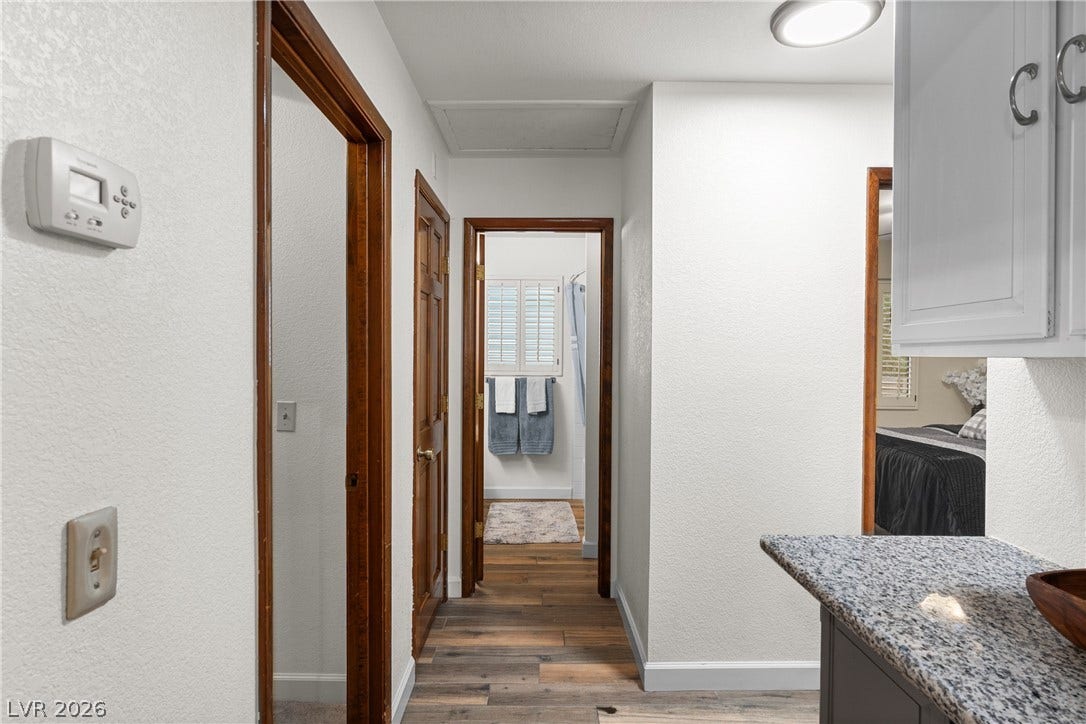 Rich wood trim frames the doorways along a hallway featuring stone countertops and laminate flooring.