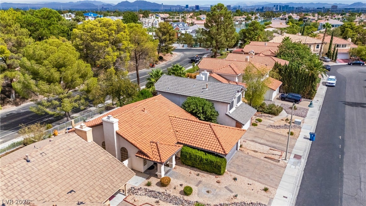 A neighborhood aerial perspective showcases tile roofing against a distant mountain and city skyline backdrop.