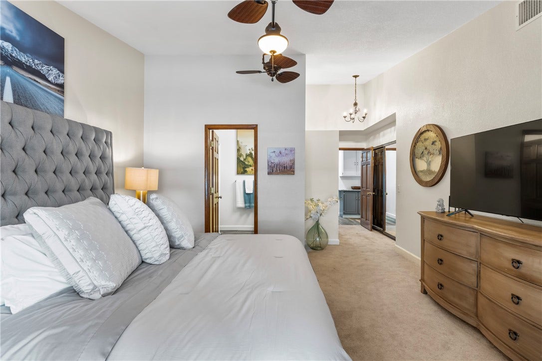 A spacious bedroom offers plush neutral carpeting and a smooth vaulted ceiling with rich wood accents.