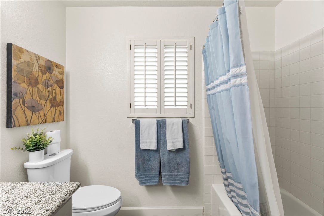 Crisp plantation shutters filter light into a bathroom featuring granite counters and tiled tub surround.