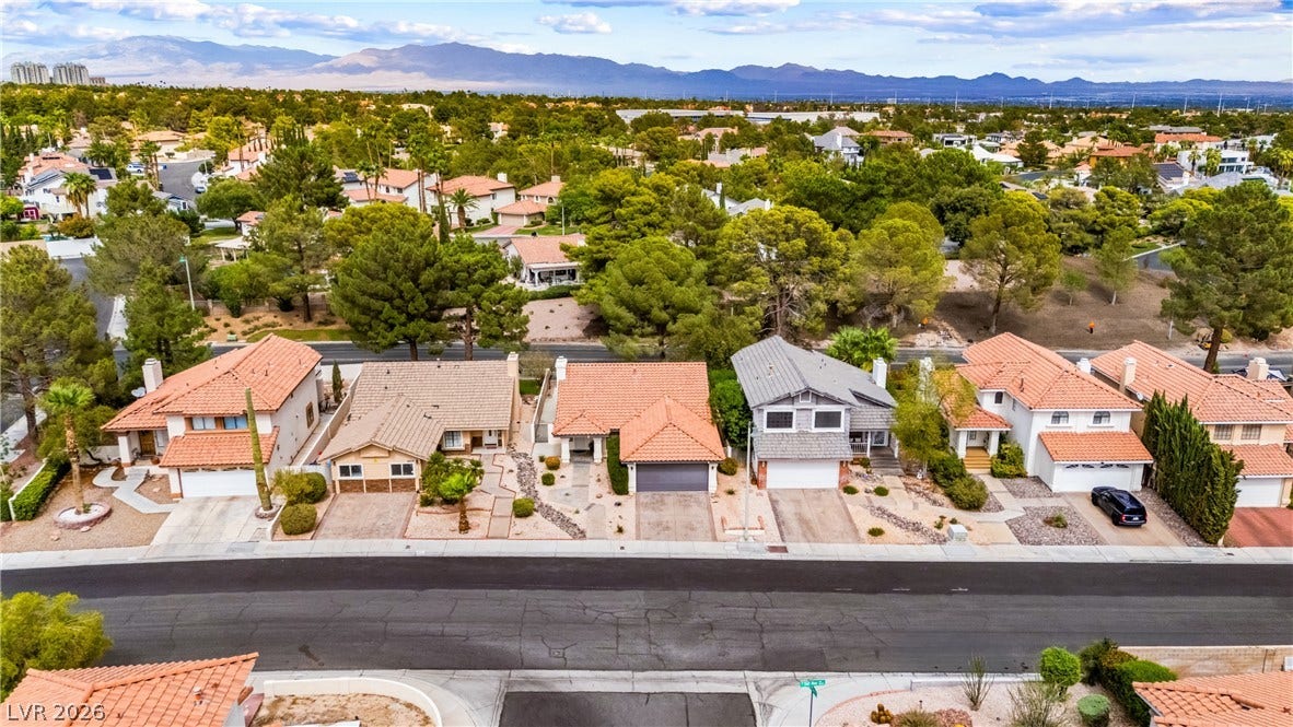 A quiet suburban streetscape captured from above displays classic tile roofs and distant mountain ridges.