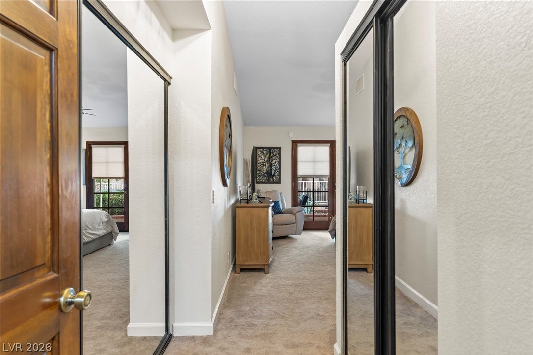 Mirrored closet doors flank a neutral carpeted hallway leading toward a bright bedroom space.
