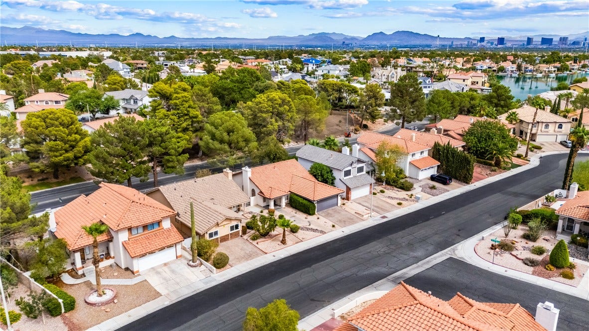 Aerial perspective showcases a quiet residential street lined with mature trees and Spanish tile roofs.